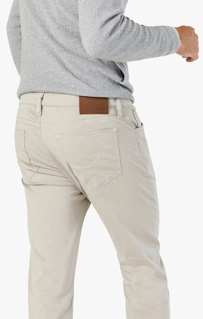A person wearing light beige pants and a light gray textured sweater, shown from the back and waist up, with one hand slightly bent and a brown patch on the pants' waistband.