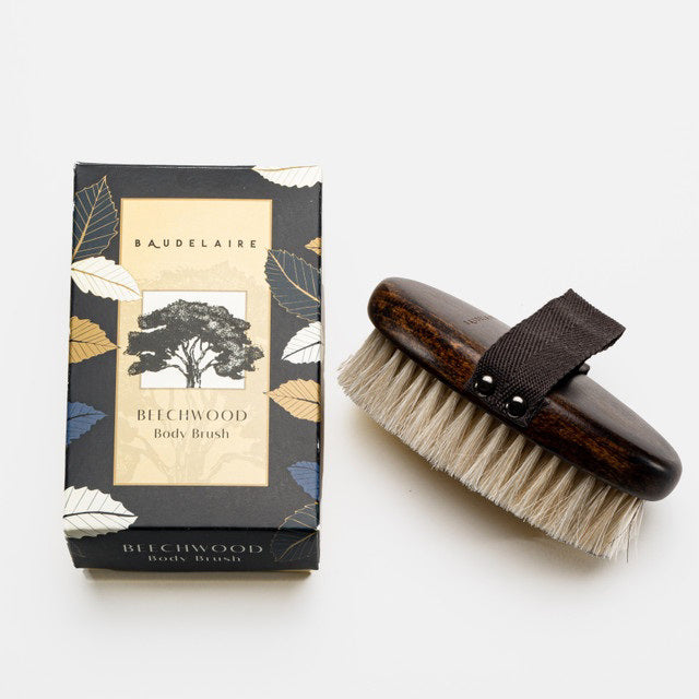 The BAUDELAIRE - BEECHWOOD 5" BODY BRUSH features a dark wooden handle, horsehair bristles, and a black fabric strap. Its box displays a tree illustration and leaf-patterned design—ideal for enhancing your self-care routine.