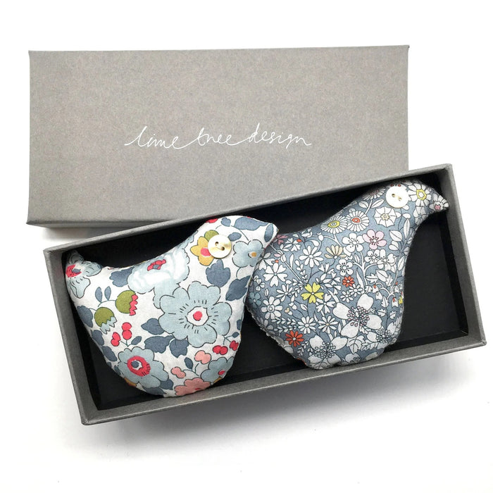 Two SONG BIRD SACHET ornaments from LIME TREE COLLECTION LTD, made with Liberty Tana Lawn floral fabrics—one blue & red, one blue & white—come side by side in a grey box, perfect as handmade lavender gifts.