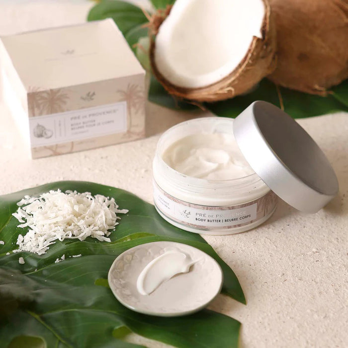 A clear plastic jar with a silver lid holds 200 ml (6.7 fl oz) of EUROPEAN SOAPS, LLC BODY BUTTER - COCONUT, enriched with Shea Butter to moisturize skin. The label indicates a coconut scent.