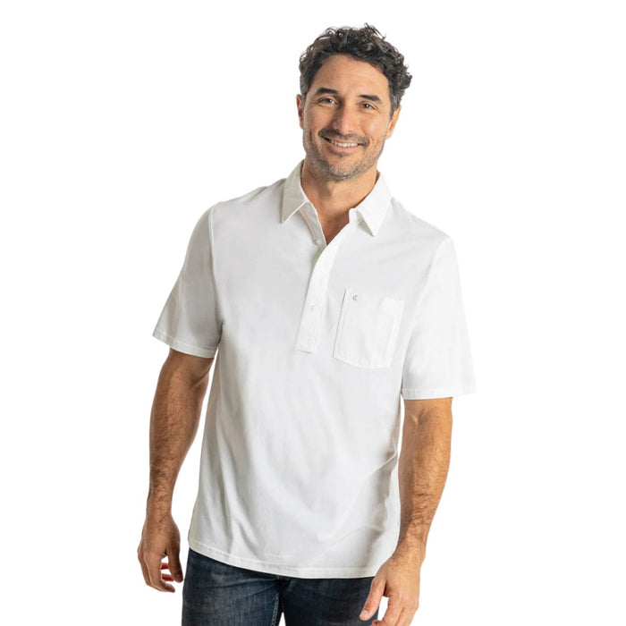 A bearded man wearing the CRIQUET Top Shelf Players Shirt in White, a classic fit short-sleeve Pima cotton shirt with a front pocket, stands against a plain light gray background.