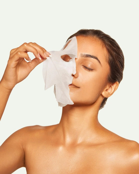 A carton labeled "ESW BEAUTY - BLUEBERRY COCONUT MILK MASK" by ESW BEAUTY sits among a milk bottle, blueberries, coconuts, and coconut flakes on white—perfect inspiration for a blueberry coconut plant-based sheet mask.