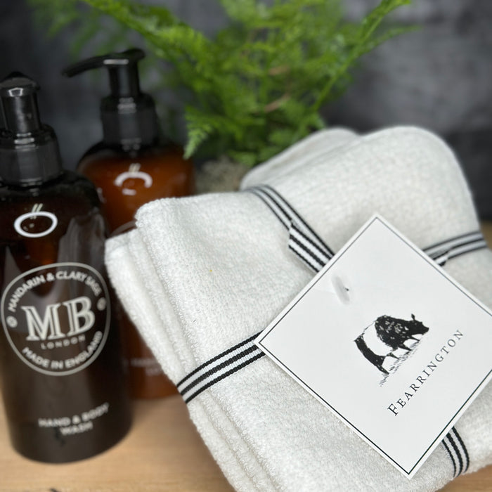 A set of four white waffle face cloths from the FEARRINGTON LIFESTYLE TOWEL COLLECTION by HARBOR LINEN, tied with a black-and-white striped ribbon and a cow-illustrated "FEARRINGTON" tag. Ideal for gentle makeup removal.