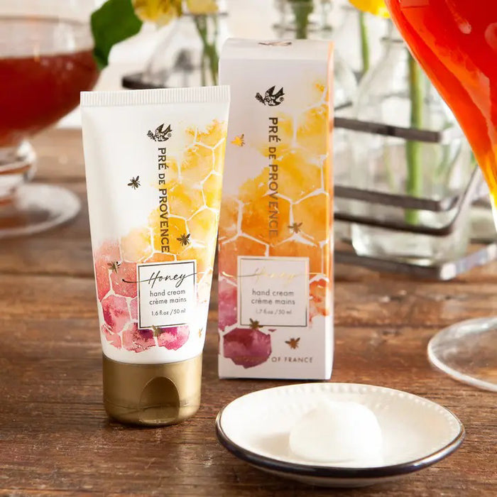 EUROPEAN SOAPS, LLC HONEY HAND CREAM (1.7 fl oz/50 ml) comes in a tube and box decorated with honeycomb, bees, and yellow-pink watercolor accents. Enriched with organic honey for deep moisture. Gold-colored text adds an elegant touch.