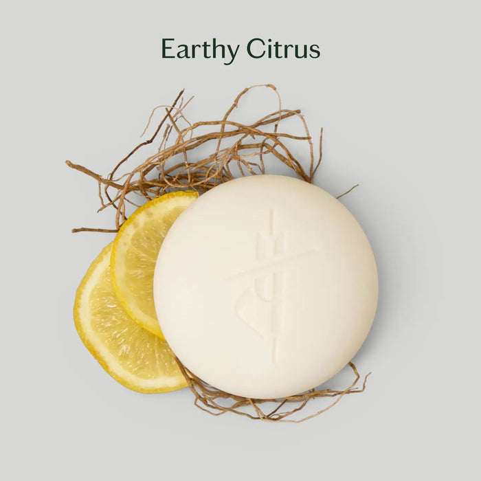 The KATE MCLEOD GROUNDING STONE MINI LOTION BAR 1OZ blends grounding vetiver root and uplifting bergamot lemon to soothe tension and nourish skin, offering a plastic-free skincare solution.