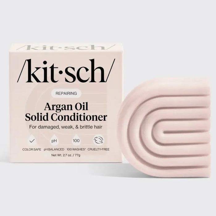 A pale pink, geometric KITSCH Argan Oil Conditioner Bar is pictured beside its box, formulated for damaged, weak, brittle hair. It’s cruelty-free, reduces frizz with argan oil, and lasts up to 100 washes.
