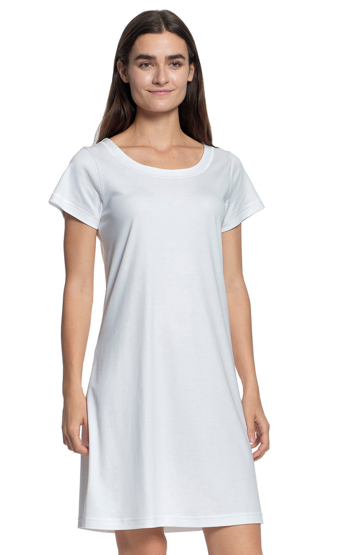 A woman with long brown hair smiles while modeling the FASHIONVIEWS P. JAMAS Butterknit Short Sleeve Gown—a light pink, knee-length pima cotton dress—against a white background.