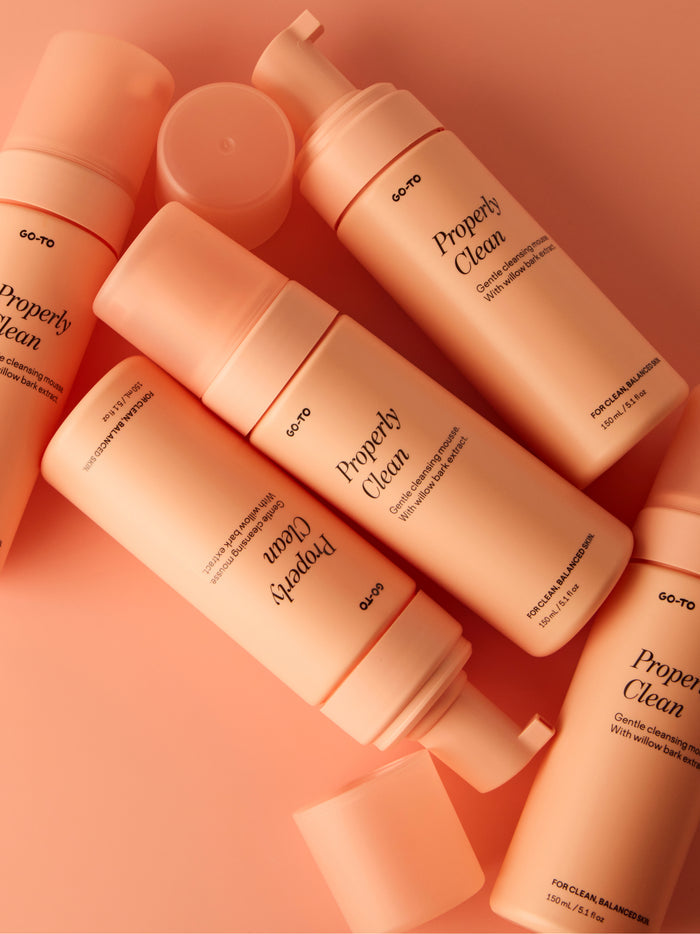 Peach-colored bottles of "Properly Clean" cleansing mousse with willow bark extract, arranged on a matching background.