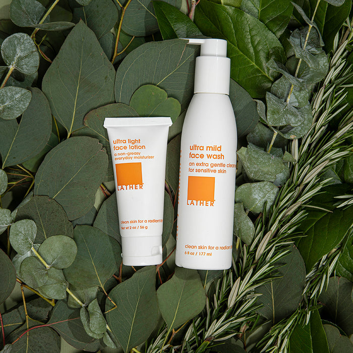 2 white bottles laid on-top of eucalyptus and rosemary leaves.