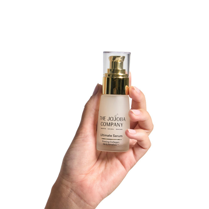 Hand holding a skincare serum bottle labeled 'The Jojoba Company' against a white background