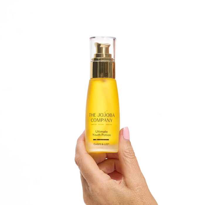 Hand holding a yellow bottle labeled 'The Jojoba Company' on a white background