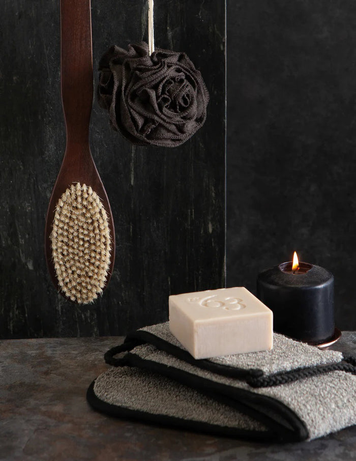 The BAMBOO CHARCOAL BACK SCRUBBER by EUROPEAN SOAPS, LLC is a gray rectangular sheath with black trim and two rope loops, designed to securely hold exfoliating tools for removing dead skin cells or unclogging pores.