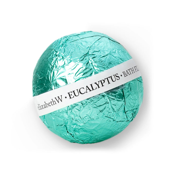 A spherical BATH FIZZ BALL EUCALYPTUS by E WIGHTMAN & CO, wrapped in shiny teal foil with a white label, releases fragrant fizz for a refreshing soak.