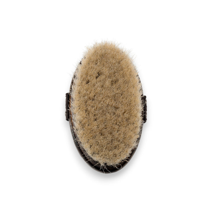 A rectangular box labeled "BAUDELAIRE - BEECHWOOD 5\" BODY BRUSH" with a tree illustration stands upright on a white surface. Next to it lies a beechwood body brush featuring natural horsehair bristles and a black hand strap. Both items evoke the essence of traditional Japanese rituals against the plain white background.