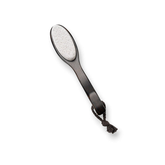 A two-sided foot file with a wooden handle and attached rope, featuring natural pumice on one side and a black abrasive surface on the other. The product, BAUDELAIRE - BEECHWOOD 8" FOOT FILE by BAUDELAIRE, is laid next to its box, which has a botanical design and the branding "Beechwood Foot File" inspired by Japanese rituals.