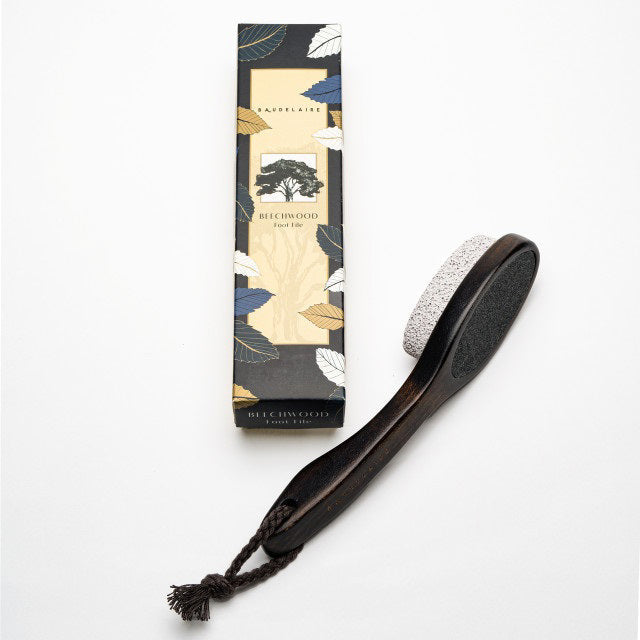 The BAUDELAIRE - BEECHWOOD 8" FOOT FILE, with a dark beechwood handle, rope loop, and natural pumice for callus removal, sits beside its leaf and tree decorated box.