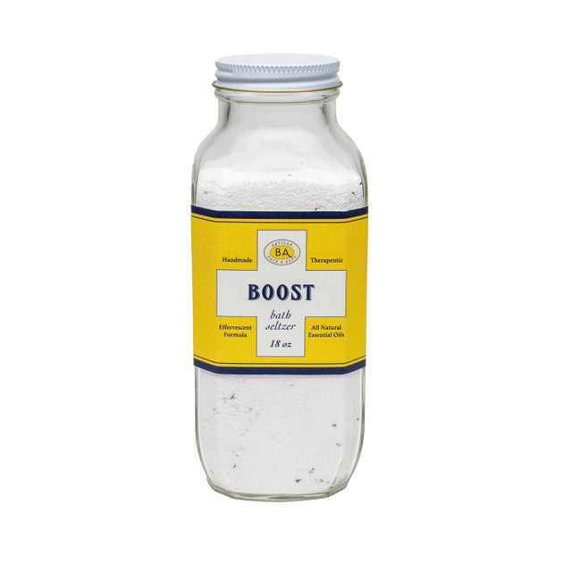 A clear glass jar labeled "BAUDELAIRE - BOOST BATH SELTZER 18OZ" contains white bath salts with essential oils. The label features "Handmade," "Therapeutic," and "All Natural Essential Oils.