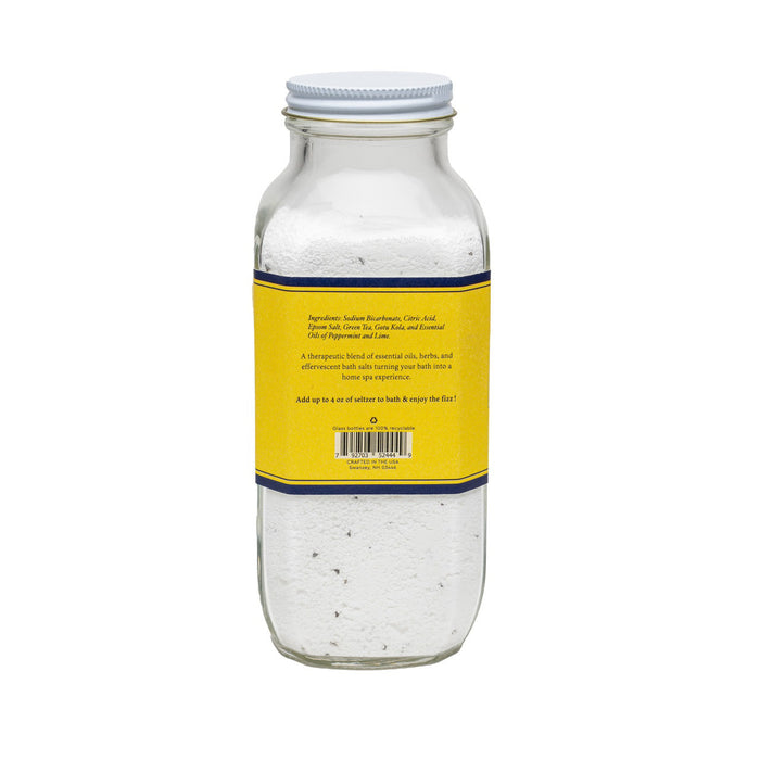 A clear glass jar labeled "BAUDELAIRE - BOOST BATH SELTZER 18OZ" contains white bath salts with essential oils. The label features "Handmade," "Therapeutic," and "All Natural Essential Oils.