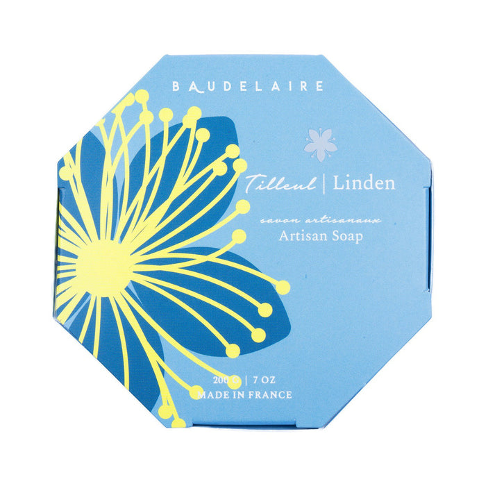 The BAUDELAIRE - LINDEN 7OZ BOXED BATH BAR comes in an octagonal blue box with a yellow and blue floral design, white text, and "Made in France" at the bottom. Enjoy its gentle shea butter formula and delicate floral scent.