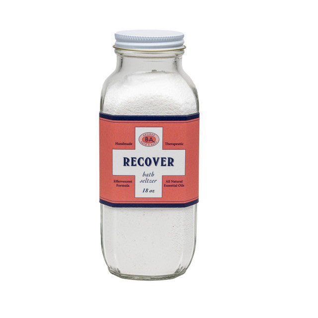 A clear glass jar of BAUDELAIRE - RECOVER BATH SELTZER 18OZ, featuring a pink and blue label, is filled with white bath salts for soothing soaks. Brand: BAUDELAIRE.