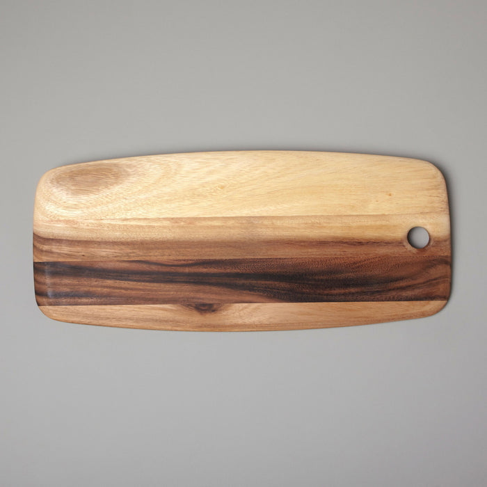 The BEHOME - ACACIA RECTANGULAR BOARD by BE HOME, INC features natural light and dark wood grain, rounded edges, and a small corner hole. It is displayed on a gray background.