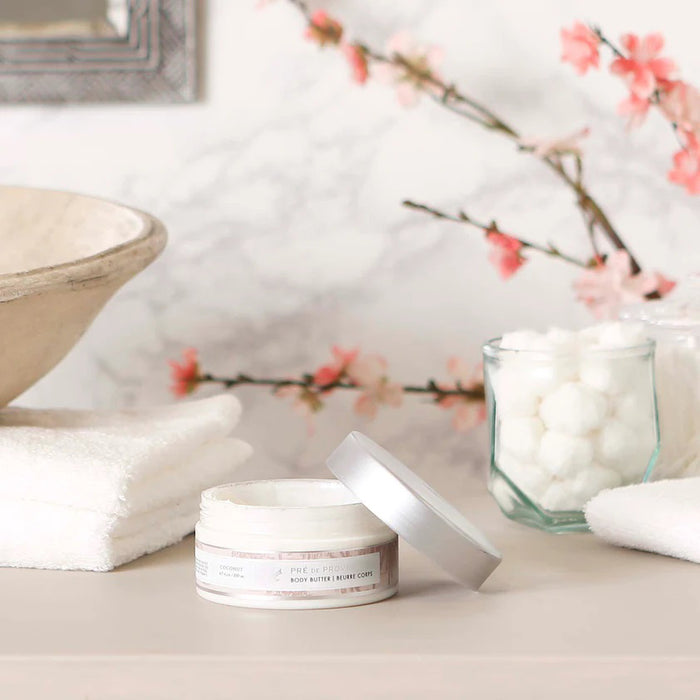 A clear plastic jar with a silver lid holds 200 ml (6.7 fl oz) of EUROPEAN SOAPS, LLC BODY BUTTER - COCONUT, enriched with Shea Butter to moisturize skin. The label indicates a coconut scent.