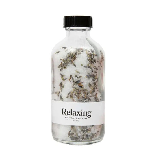 A clear glass jar with a black lid holds GIFTEN MARKET's BOTANICAL BATH SOAK - RELAXING, a white detox blend with dried lavender peppermint. The label reads "BOTANICAL BATH SOAK - RELAXING.