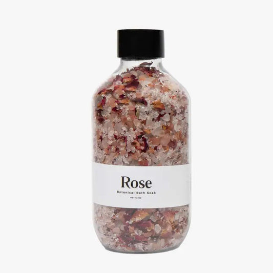 A clear bottle from GIFTEN MARKET holds pink and white BOTANICAL BATH SOAK - ROSE with dried rose petals. The label displays "Rose Botanical Bath Soak" on a white background.