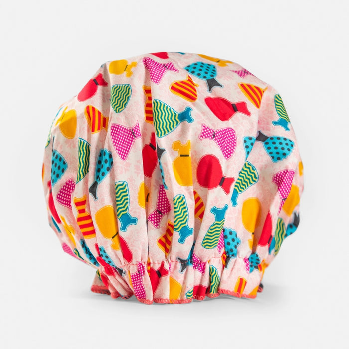 A colorful, waterproof bouffant shower cap from BATH ACCESSORIES COMPANY, called the “BOUFFANT SHOWER CAP - CUPCAKES,” featuring a playful cupcake pattern on a white background and gathered with elastic at the base, displayed against a plain white surface.