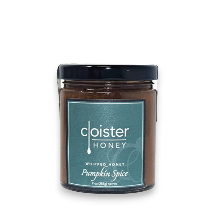 A jar of Cloister Honey's Whipped Honey Pumpkin Spice, adorned with a black lid and teal label, sits elegantly on a white surface. Its 9 oz (255g) size allows reflections to shimmer around its inviting charm.