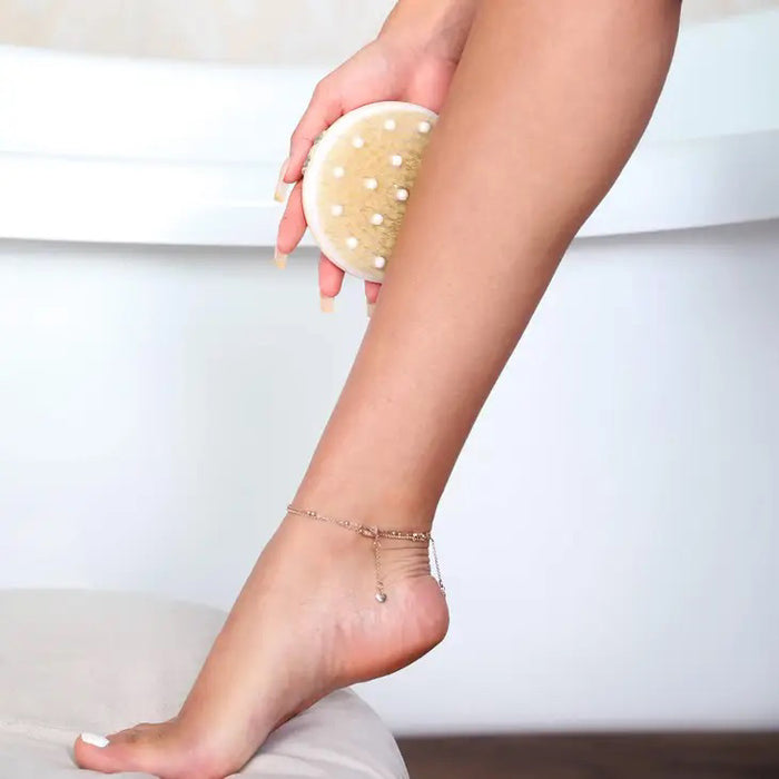 The DAILY CONCEPTS DETOX MASSAGE BRUSH, featuring natural bristles, is shown next to its clear packaging that highlights benefits like dry brushing for smoother, more radiant skin and helping reduce cellulite.