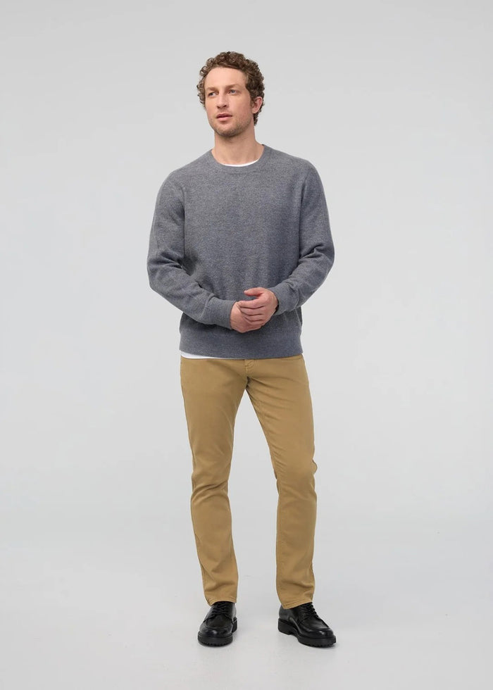 A man with short dark hair and a trimmed beard stands against a white background, wearing a white t-shirt, white sneakers with black details, and DUER's DU/ER NO SWEAT RELAXED TAPER PANT in an athletic fit. One hand is in his pocket.