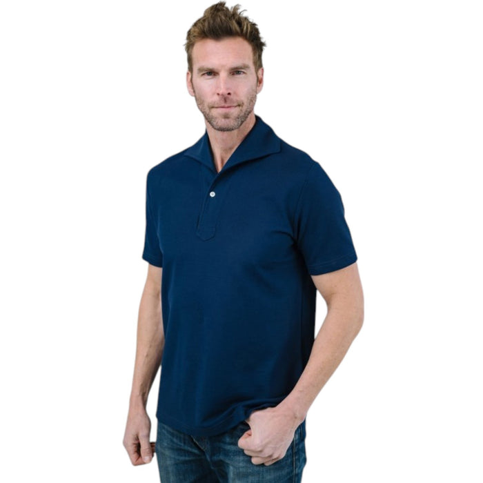 A man with light brown hair and a short beard wears the EDWARD ARMAH Pima Cotton Tailored Polo Shirt in dark blue and jeans, standing against a plain light background with a relaxed expression and one hand in his pocket.