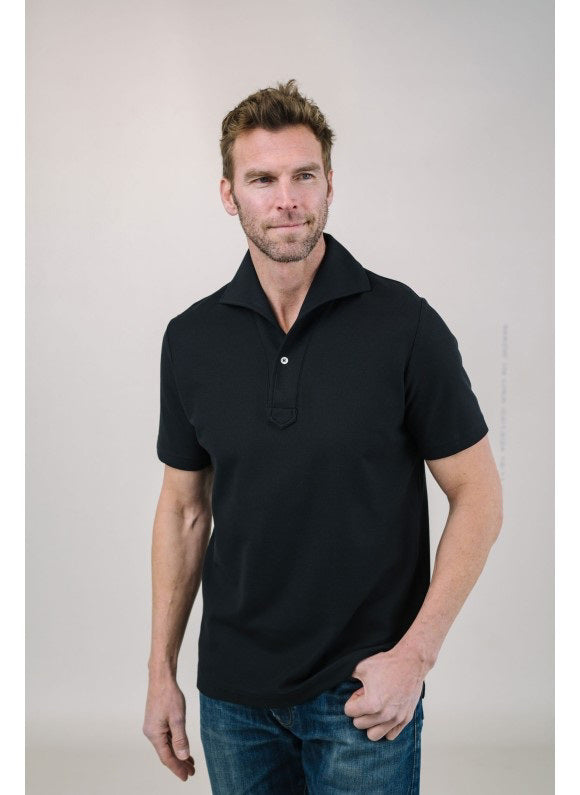 A man with light brown hair and a short beard wears the EDWARD ARMAH Pima Cotton Tailored Polo Shirt in dark blue and jeans, standing against a plain light background with a relaxed expression and one hand in his pocket.