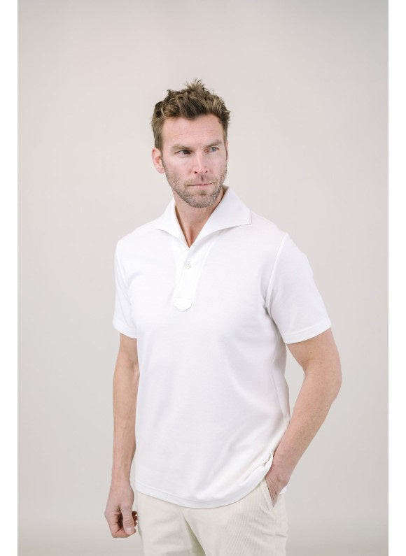 A man with light brown hair and a short beard wears the EDWARD ARMAH Pima Cotton Tailored Polo Shirt in dark blue and jeans, standing against a plain light background with a relaxed expression and one hand in his pocket.