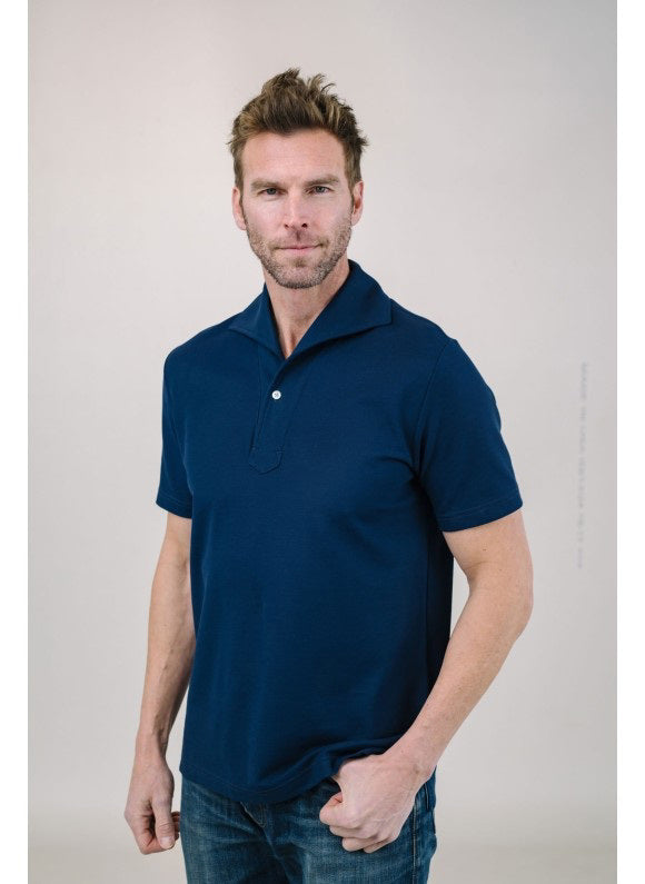 A man with light brown hair and a short beard wears the EDWARD ARMAH Pima Cotton Tailored Polo Shirt in dark blue and jeans, standing against a plain light background with a relaxed expression and one hand in his pocket.