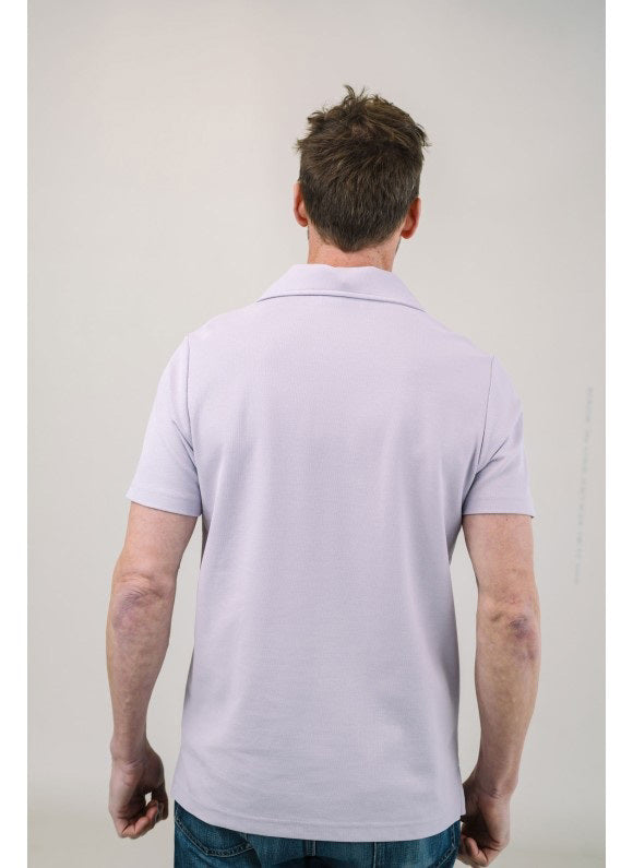 A man with light brown hair and a short beard wears the EDWARD ARMAH Pima Cotton Tailored Polo Shirt in dark blue and jeans, standing against a plain light background with a relaxed expression and one hand in his pocket.