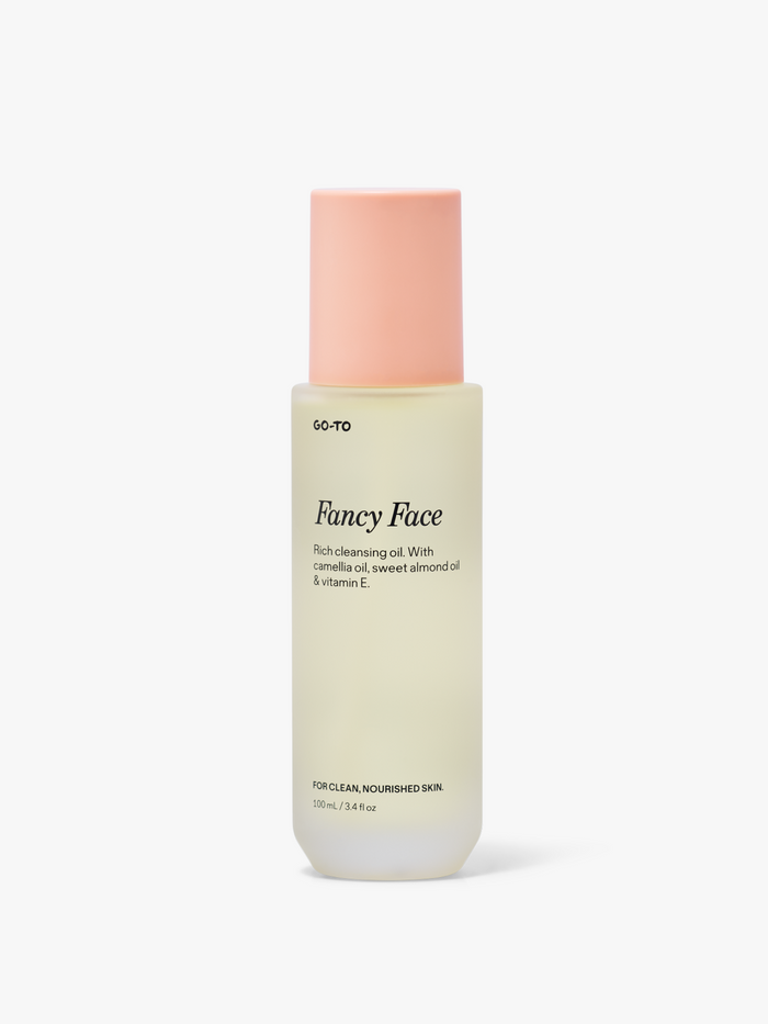 A bottle of Fancy Face cleansing oil with a peach cap, featuring camellia oil, sweet almond oil, and vitamin E for nourished skin