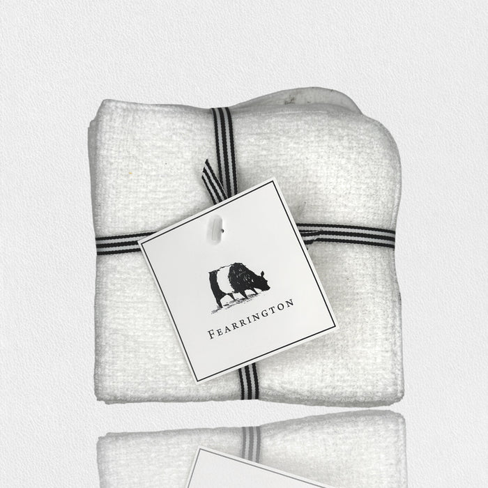 A set of four white waffle face cloths from the FEARRINGTON LIFESTYLE TOWEL COLLECTION by HARBOR LINEN, tied with a black-and-white striped ribbon and a cow-illustrated "FEARRINGTON" tag. Ideal for gentle makeup removal.