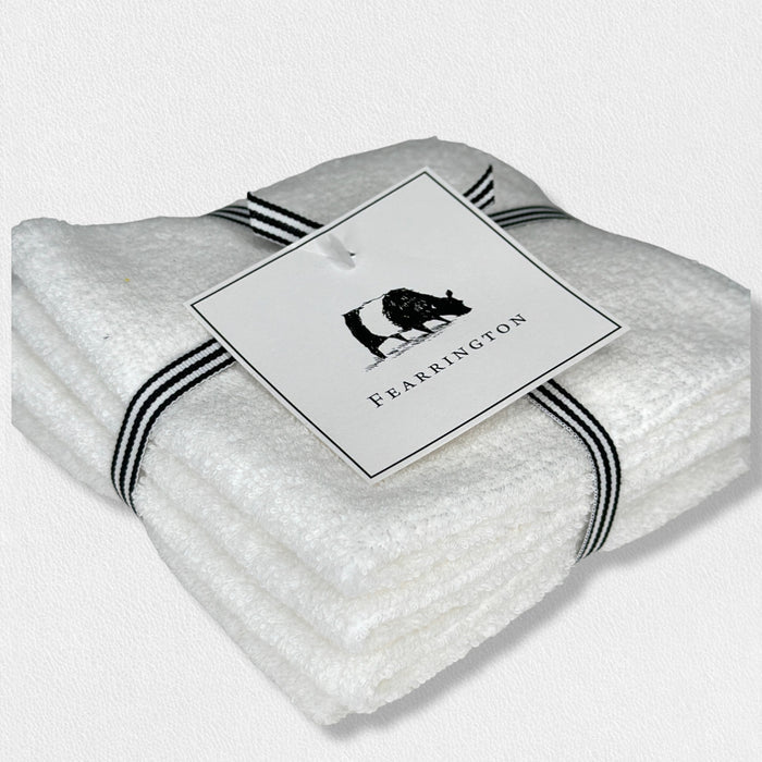 A set of four white waffle face cloths from the FEARRINGTON LIFESTYLE TOWEL COLLECTION by HARBOR LINEN, tied with a black-and-white striped ribbon and a cow-illustrated "FEARRINGTON" tag. Ideal for gentle makeup removal.