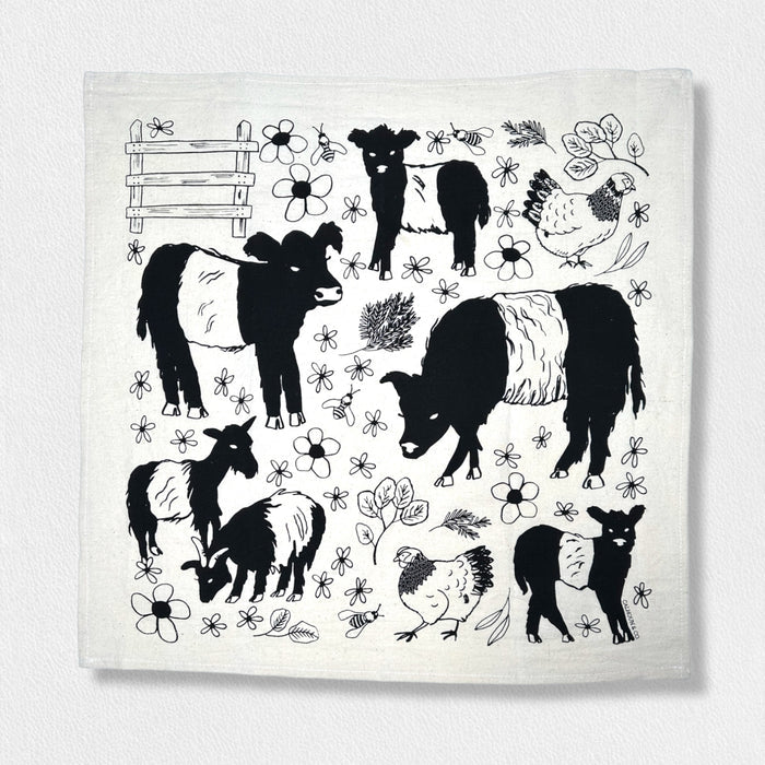 The CALHOUN & CO. FEARRINGTON SIGNATURE COLLECTION - BESPOKE BELTIE BARNYARD TEA TOWEL features black, hand-drawn belted cows, goats, and chickens with florals and a wooden fence, capturing the charm of Fearrington Village.
