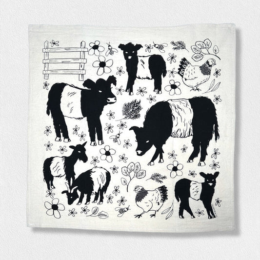 The CALHOUN & CO. FEARRINGTON SIGNATURE COLLECTION - BESPOKE BELTIE BARNYARD TEA TOWEL features black, hand-drawn belted cows, goats, and chickens with florals and a wooden fence, capturing the charm of Fearrington Village.