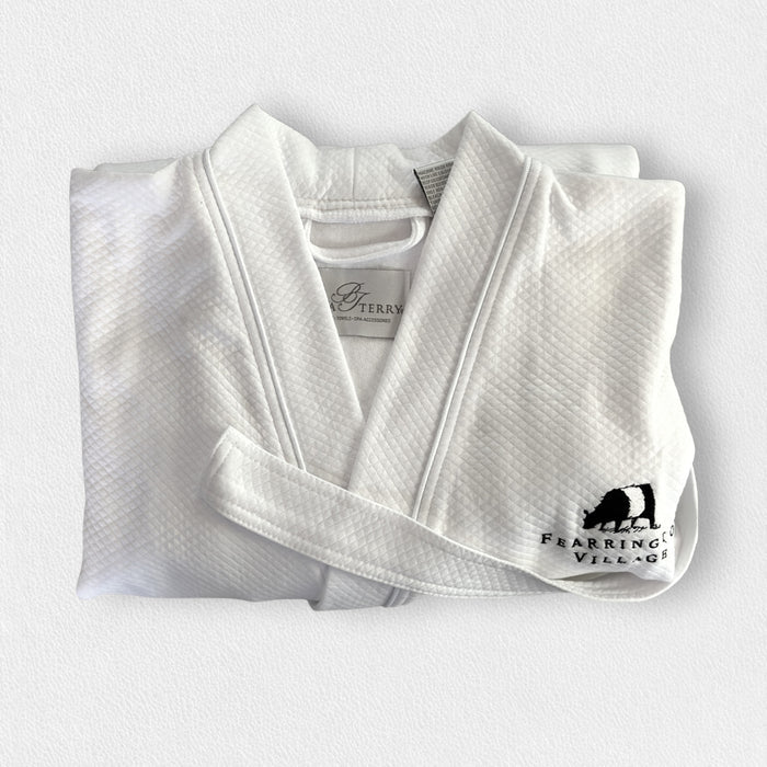The BOCA FEARRINGTON SIGNATURE COLLECTION - FEARRINGTON VILLAGE ROBE is a folded white waffle-knit kimono collar bathrobe featuring a black bear logo and "Fearrington Village" embroidered on the chest, displayed on a light textured surface.