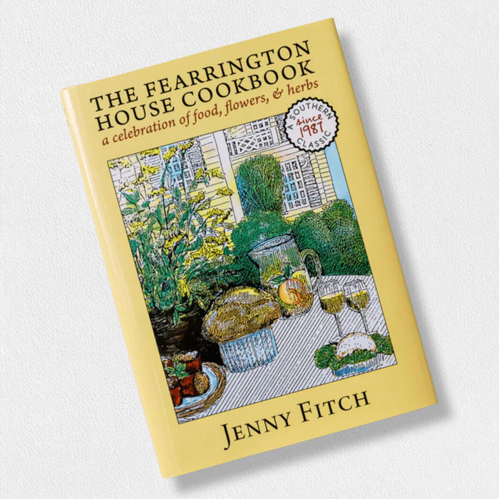 The FEARRINGTON SIGNATURE COLLECTION – THE FEARRINGTON HOUSE COOKBOOK BY JENNY FITCH from BELTED GOAT features an illustrated cover with an outdoor table set with food, wine, and flowers against a yellow border—celebrating Southern cuisine and hospitality.