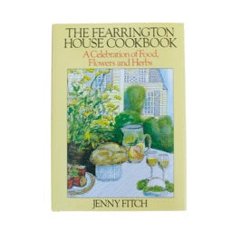 The FEARRINGTON SIGNATURE COLLECTION – THE FEARRINGTON HOUSE COOKBOOK BY JENNY FITCH from BELTED GOAT features an illustrated cover with an outdoor table set with food, wine, and flowers against a yellow border—celebrating Southern cuisine and hospitality.