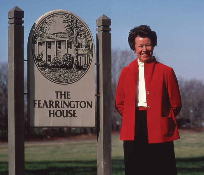 The FEARRINGTON SIGNATURE COLLECTION – THE FEARRINGTON HOUSE COOKBOOK BY JENNY FITCH from BELTED GOAT features an illustrated cover with an outdoor table set with food, wine, and flowers against a yellow border—celebrating Southern cuisine and hospitality.