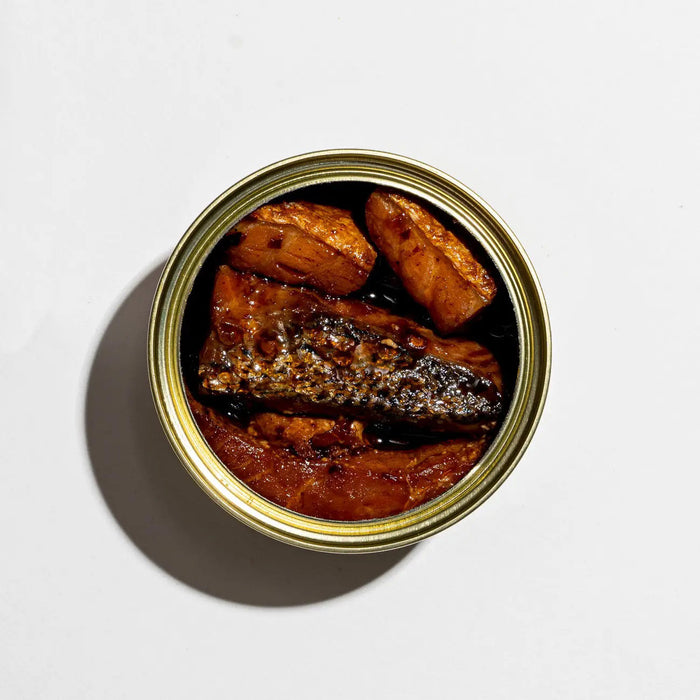 A vibrant design of the FISHWIFE tin shows a woman with salmon on her head, surrounded by fish and bowls. The text reads, "Smoked Salmon with Fly By Jing Sichuan Chili Crisp," responsibly raised in Norway for exceptional quality and taste.