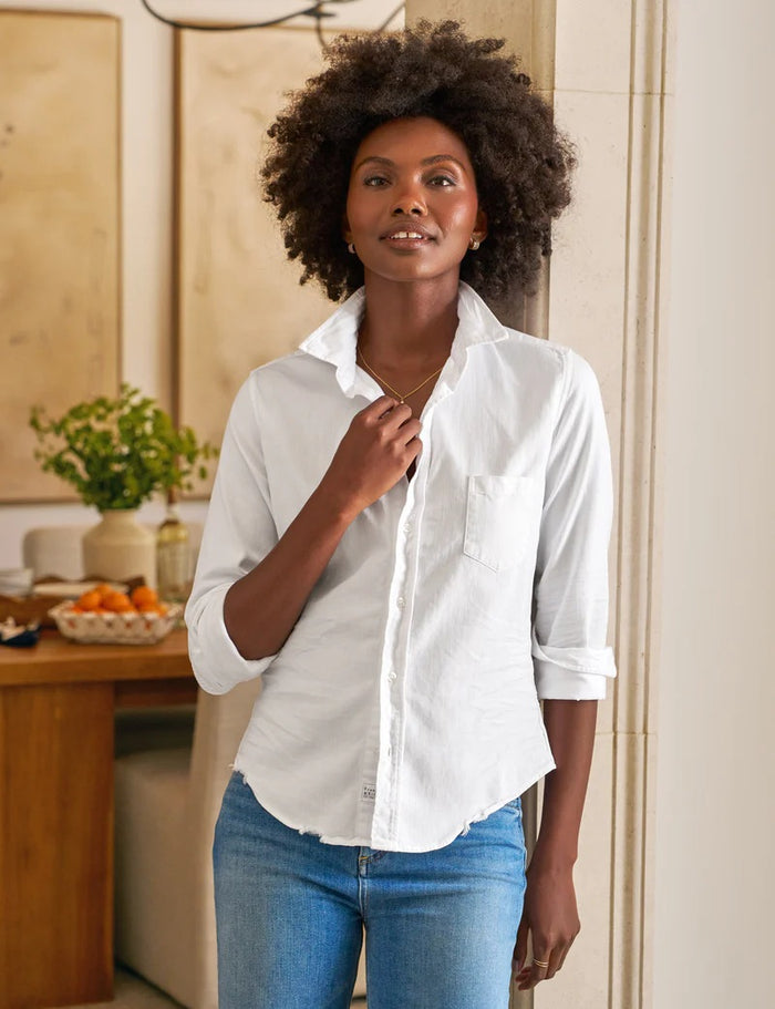 The FRANK & EILEEN Barry Tailored Button Up in Famous Denim White features long rolled sleeves, a single chest pocket, and a curved hem, shown against a textured white background.