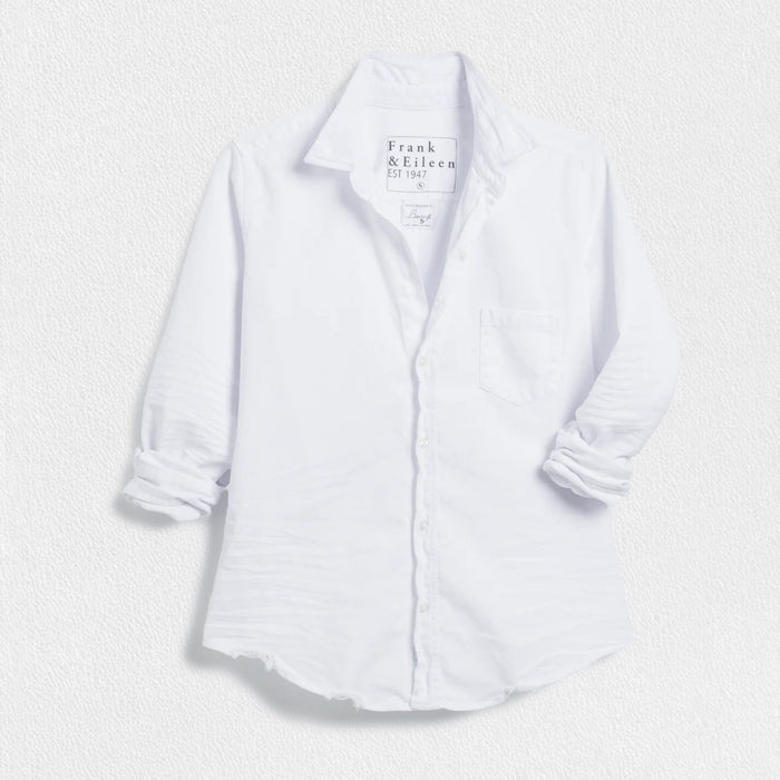The FRANK & EILEEN Barry Tailored Button Up in Famous Denim White features long rolled sleeves, a single chest pocket, and a curved hem, shown against a textured white background.