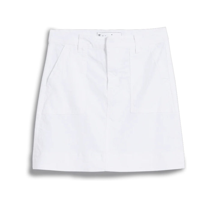 A person stands outdoors with one hand in the utility pocket of the FRANK & EILEEN Jameson Utility Skirt in Performance Linen White, paired with a long-sleeve black-and-white striped shirt. Greenery and sunlight fill the background.